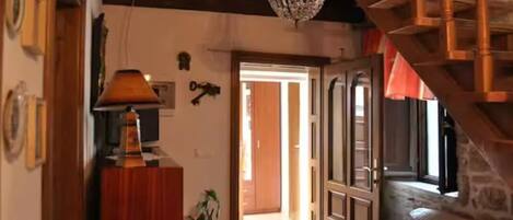 A room with a wooden ceiling, a chandelier, a wooden staircase, and a door leading outside.