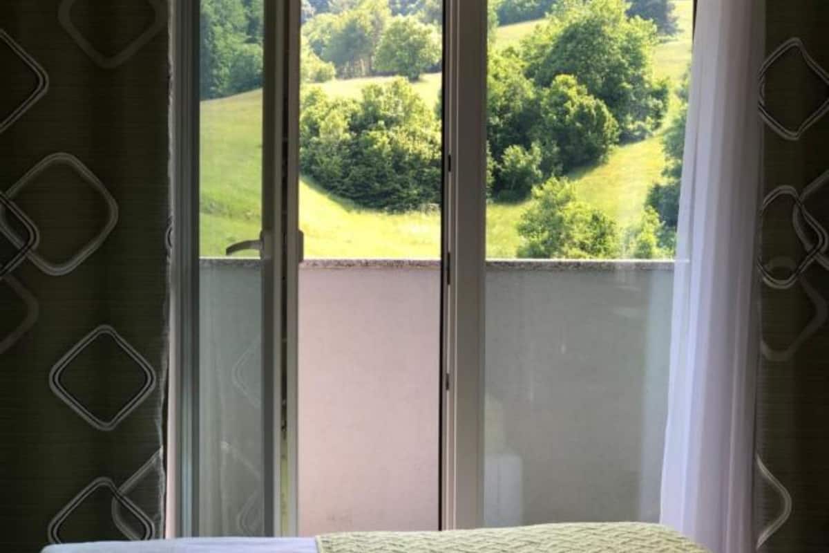Una habitación con vistas a un paisaje verde a través de una ventana con cortinas.