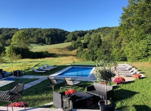 A swimming pool with lounge chairs, a barbecue area, and a view of a forested hillside.
