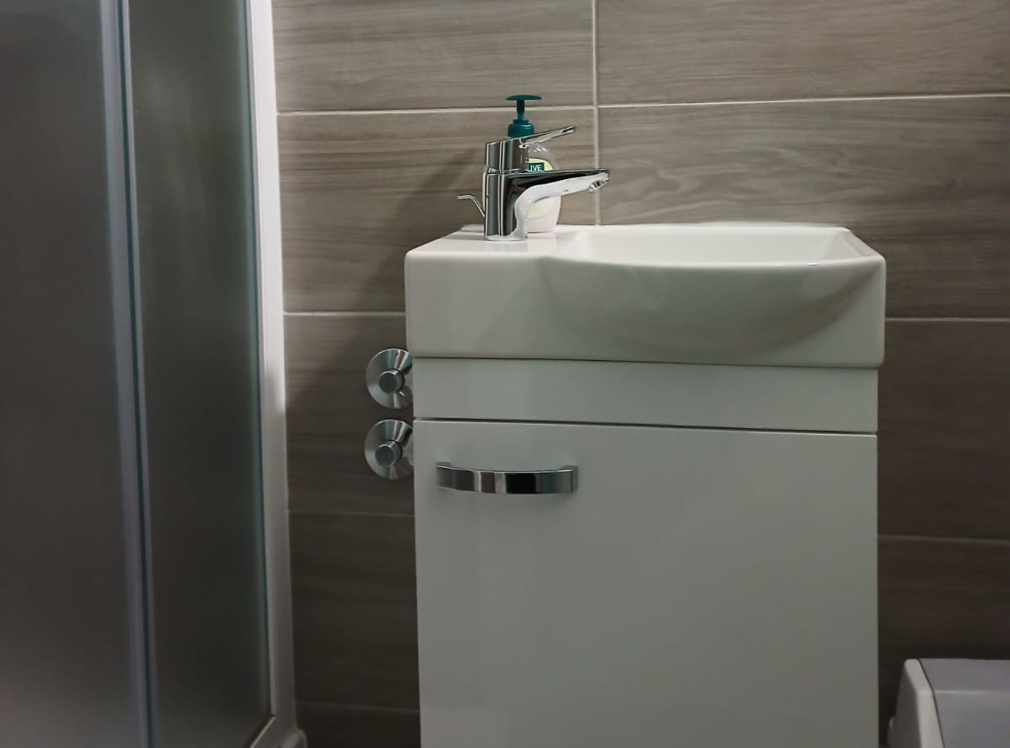 Un baño con un lavamanos blanco, dispensador de jabón y un inodoro.