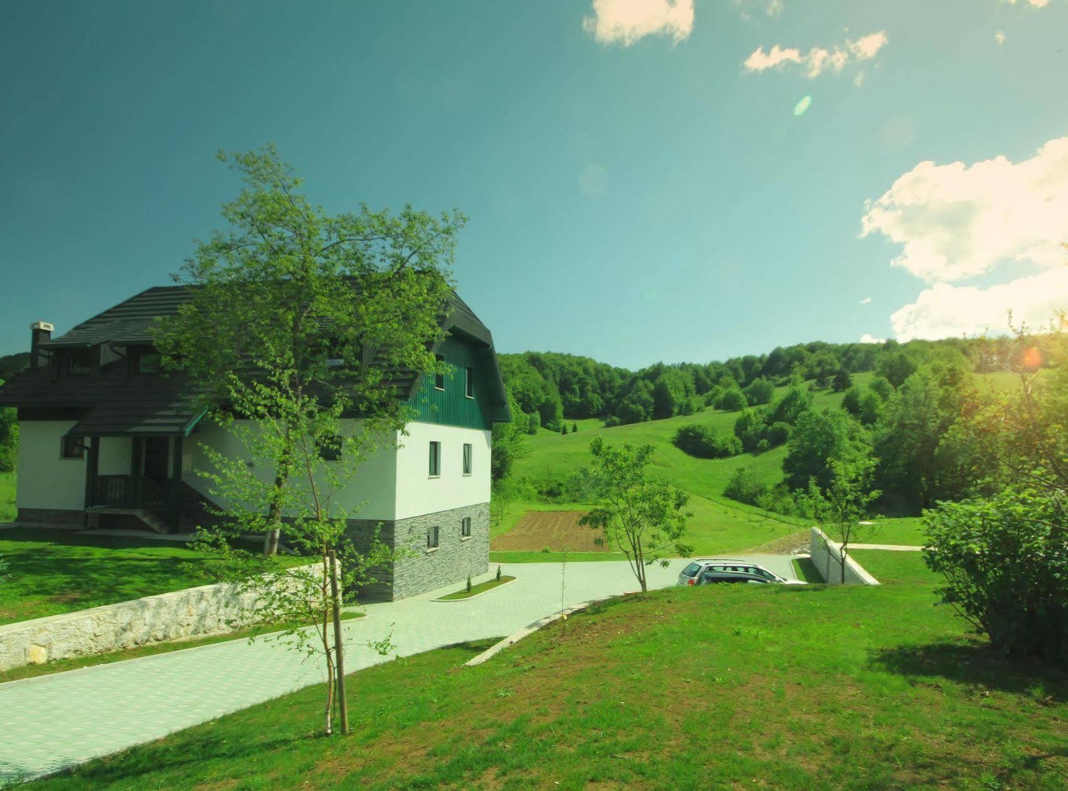 A house with a stone foundation, a green roof, and a paved driveway.