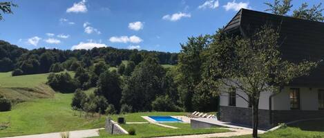 Una casa con piscina, rodeada de césped y árboles.
