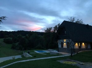 A house with a sloped roof, a swimming pool, and a paved pathway leading to the entrance.
