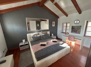 Une chambre Ă coucher avec un grand lit, une table de chevet, une chaise, un bureau et un miroir.