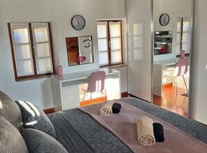 A bedroom with a bed, a desk, a chair, a mirror, and a clock on the wall.