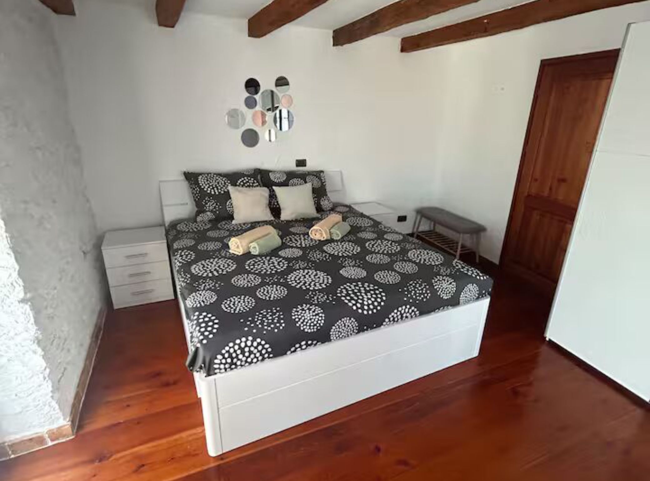 A bedroom with a bed, bedside tables, a bench, and a wall with decorative mirrors.