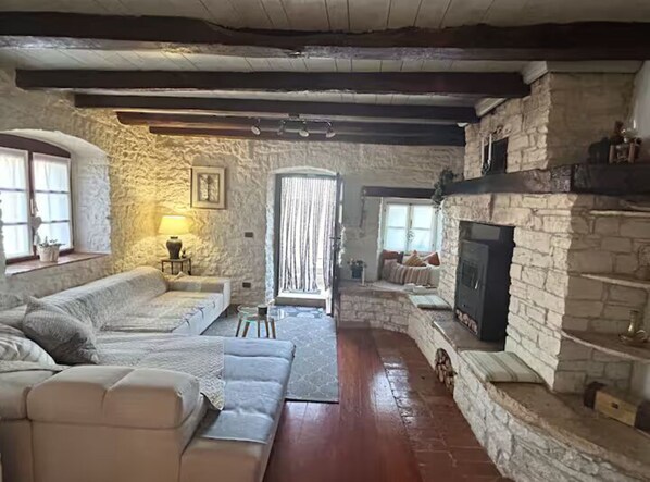 A rustic stone interior with a fireplace, a sofa, and a window.