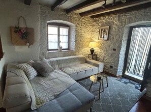 A cozy room with a sofa, a small table, a lamp, a window, and a stone wall.