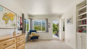 Ein Zimmer mit einem Holzkasten, einem blauen Sessel, einer Karte an der Wand und einem Bücherregal.