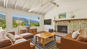 Ein Wohnzimmer mit Kamin, Ledersofas, einem Couchtisch und Bergblick durch große Fenster.