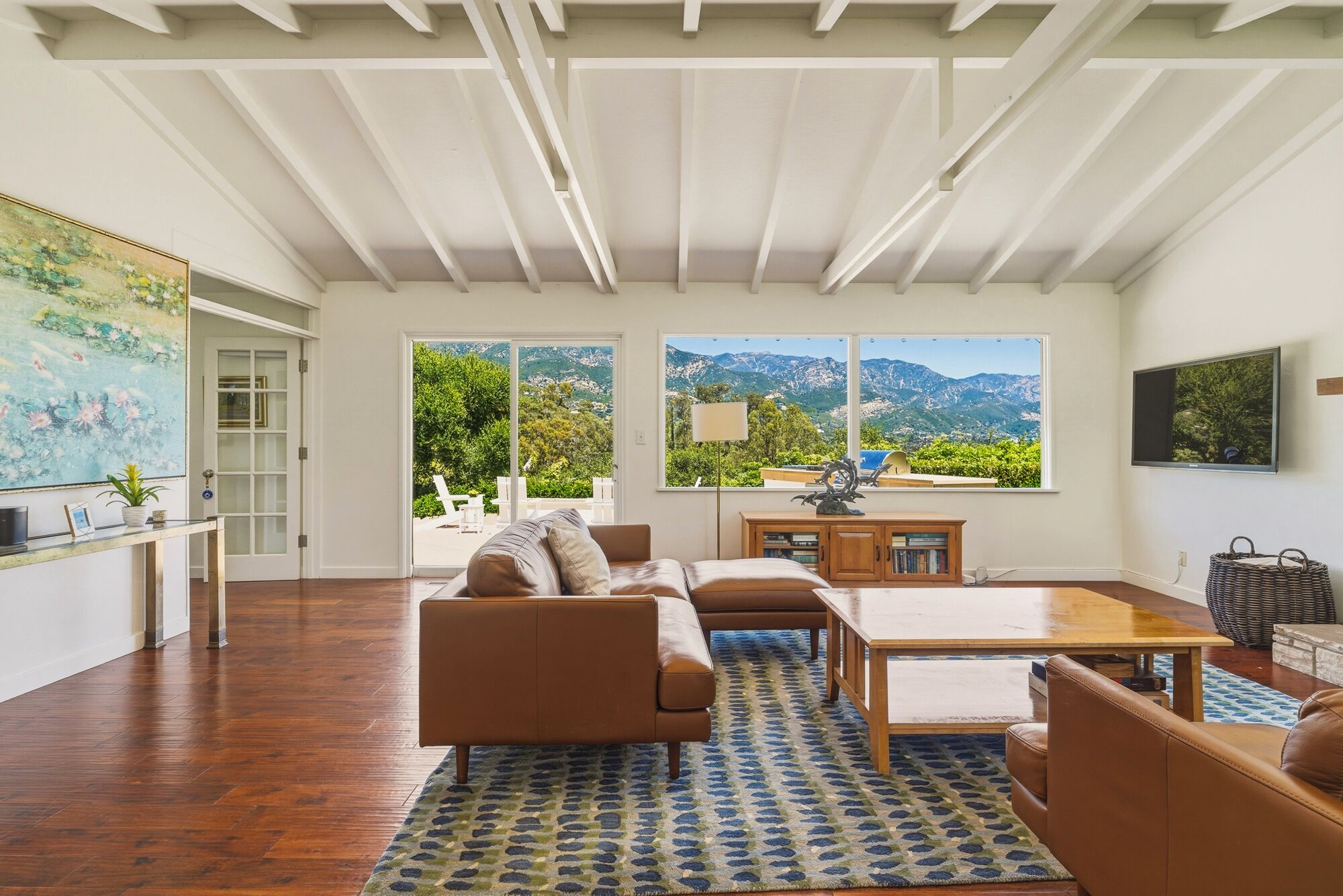 A spacious living room with a large window, a sofa, a coffee table, and a view of mountains.