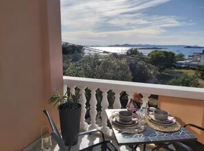 A balcony with a table set for dining, overlooking a scenic view of a body of water and distant land.