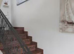 Una escalera con barandilla, un cuadro de un velero en la pared, y un estante con un adorno.