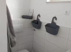 A bathroom with white tiled walls, two wall-mounted sinks, a towel rack, and a small shelf with a book. - Villa Meeresblick (Pakostane)