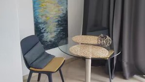 A modern room with a glass table, a chair, a painting, and a curtain.