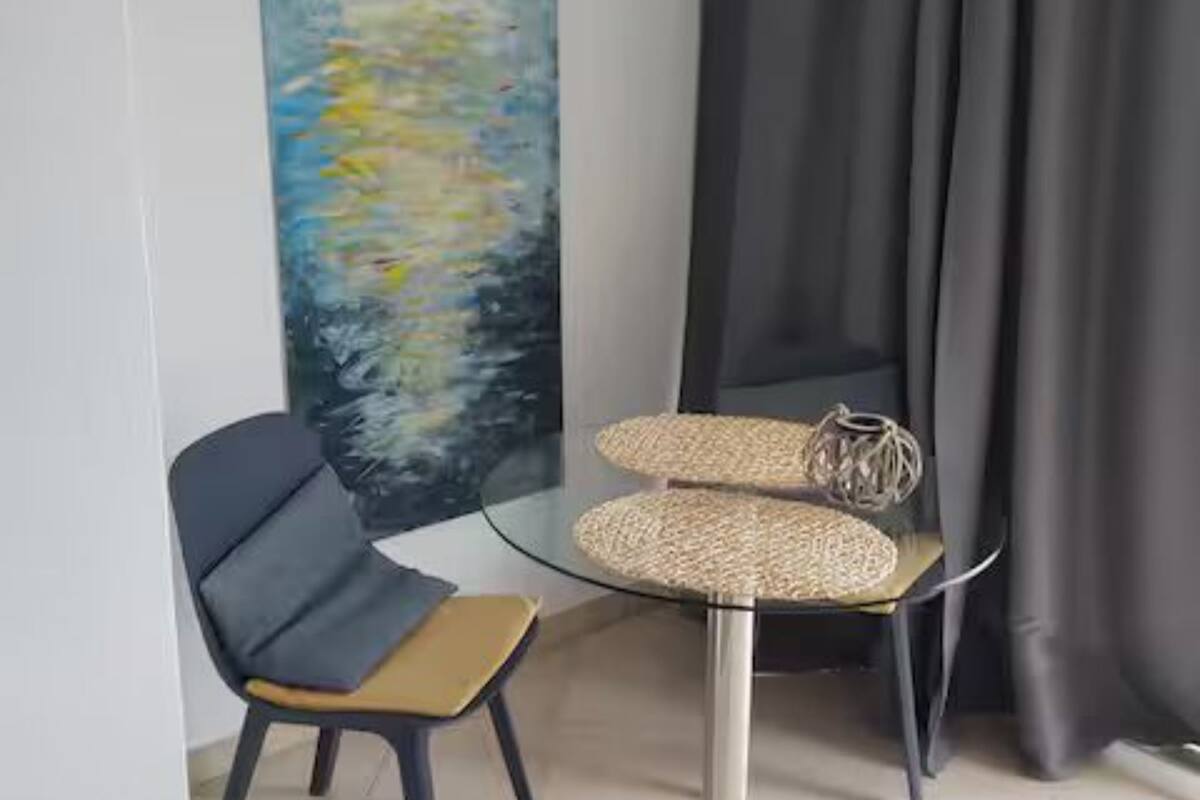 Una habitación moderna con una mesa de vidrio, una silla, un cuadro y una cortina.