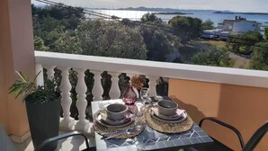 A balcony with a table set for two, overlooking a scenic view of a body of water and distant land.