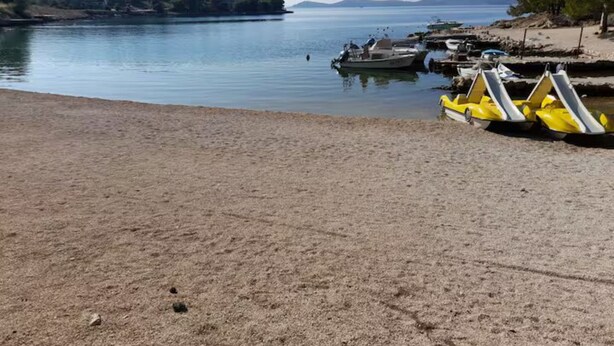 A beach with boats, a calm lake, and a distant shoreline.