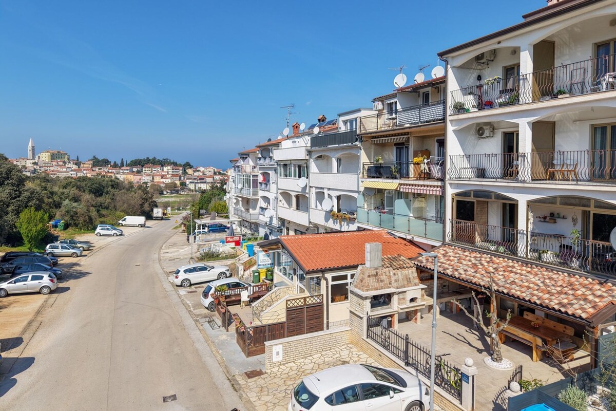 A coastal town with multi-story buildings, a street with parked cars, and a clear blue sky.