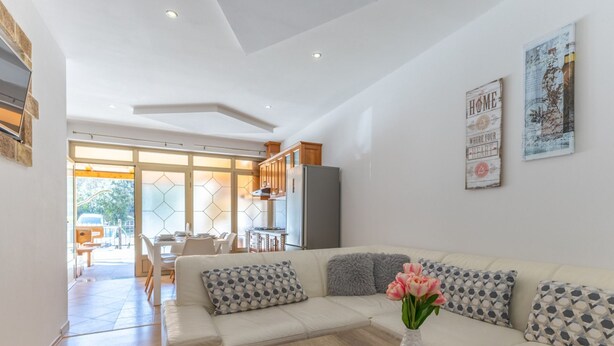 A modern living room with a sectional sofa, a coffee table, and a vase with flowers. There is a dining area in the background with a table and chairs. - A.m. Apartments (Vrsar)