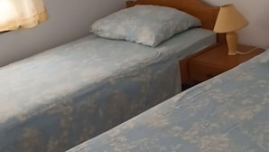 Uma cama de casal com peseira de madeira, mesa de cabeceira com abajur e janela com cortina.