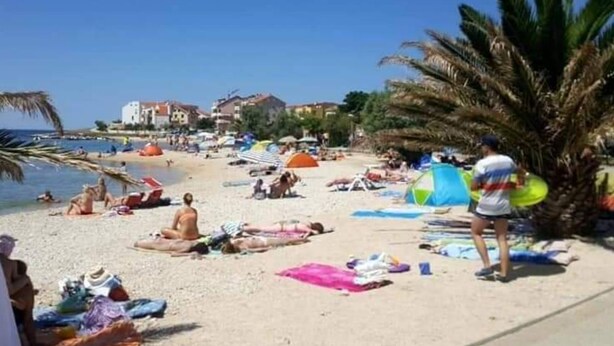 Uma praia com pessoas se banhando ao sol, guarda-sóis e tendas.