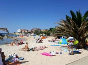 A beach with people sunbathing, umbrellas, and tents. - Apartments Cvetnić (Povljana)