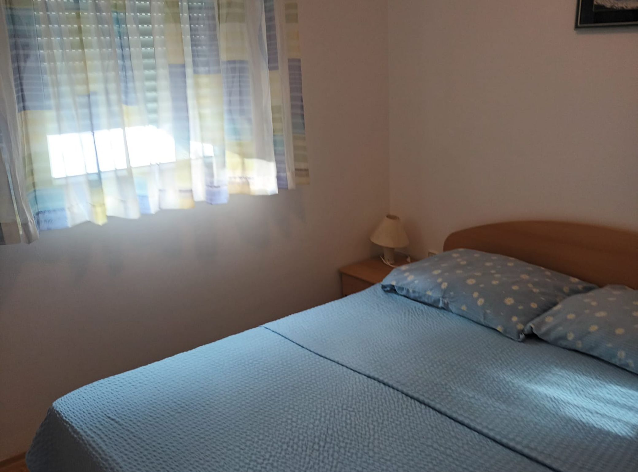 A bedroom with a bed, a nightstand, a lamp, and a window with curtains.
