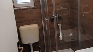 Box de vidro com chuveiro, vaso sanitário e janela acima.
