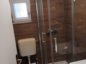 A modern bathroom with a glass-enclosed shower, a toilet, and a window above the toilet. - Apartments Cvetnić (Povljana)