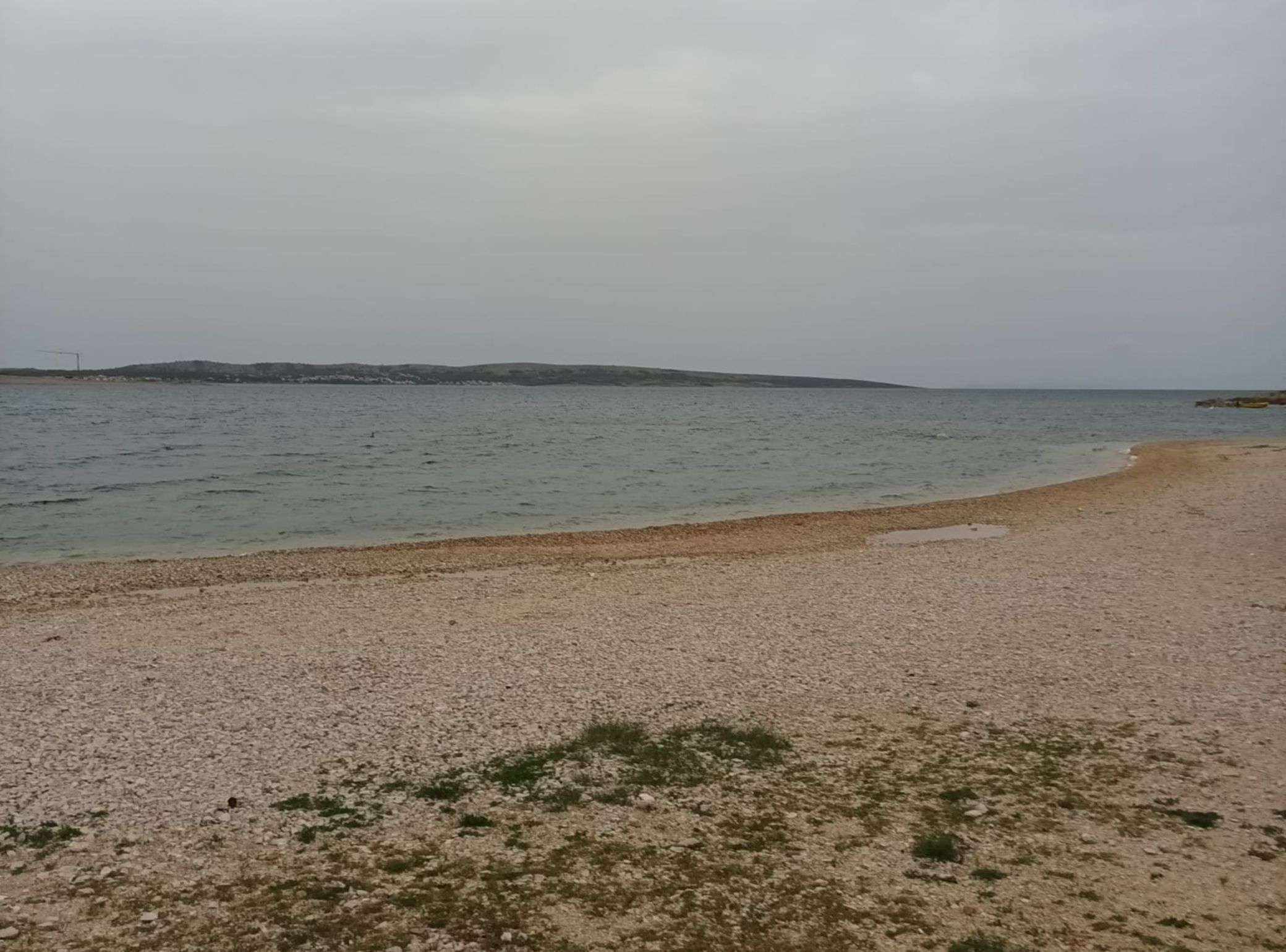 Ein Kiesstrand mit ruhigem Wasser und sanften Hügeln im Hintergrund.