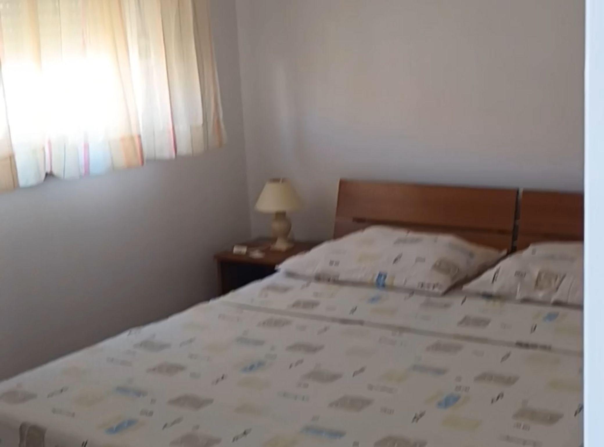 A room with a bed, a nightstand with a lamp, and a window with curtains.