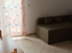 A room with a sofa, a table, and a curtain with a pattern. - Apartments Cvetnić (Povljana)