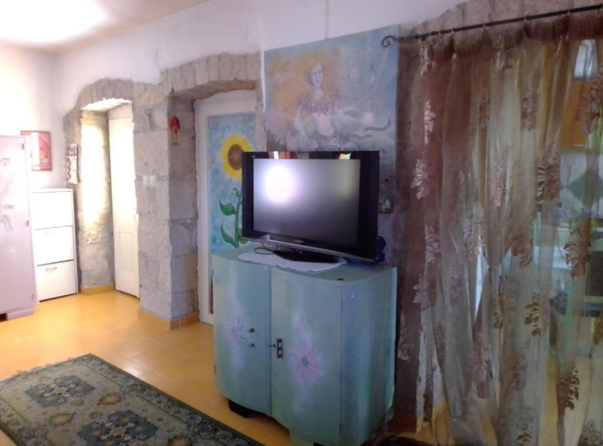 A room with a television on a cabinet, a door with a painting, and a patterned rug.