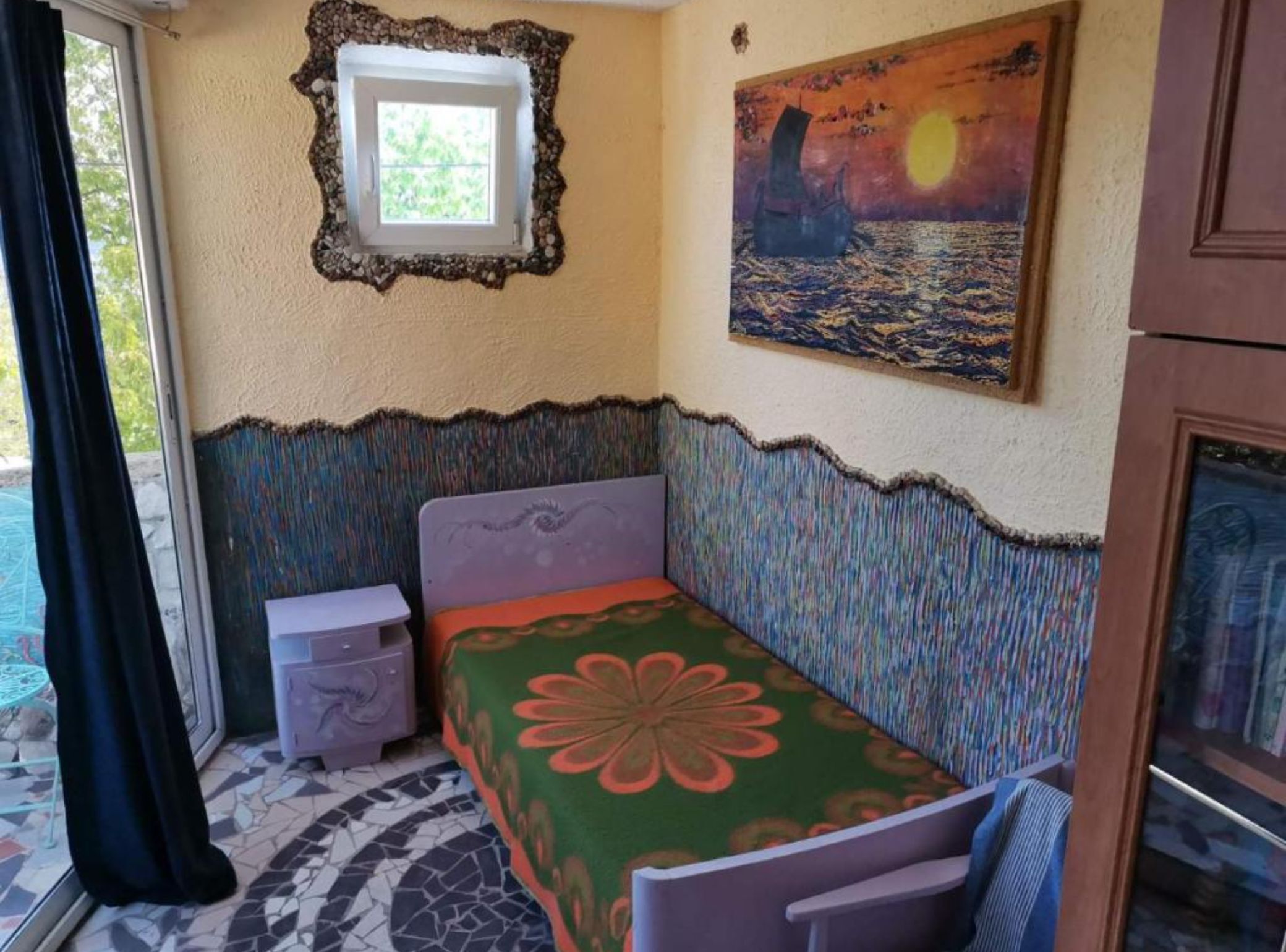 Een kamer met een bed, een tafeltje, een raam en een schilderij aan de muur.
