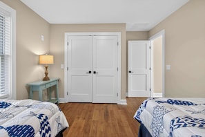 A bedroom with two beds, a wardrobe, a nightstand with a lamp, and a window with blinds. - Newly Built Cozy Delaware Home (Ocean View)