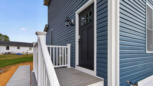 Una casa con fachada azul oscuro, puerta principal blanca y un pequeño porche con barandilla blanca.