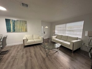 Ein Wohnzimmer mit zwei weißen Sofas, einem Glastisch und einem großen abstrakten Gemälde an der Wand.