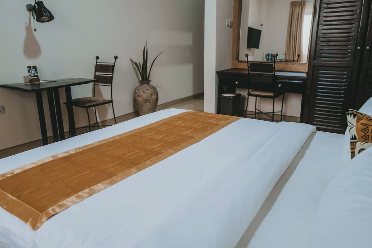 Una habitación de hotel con cama, escritorio, silla, espejo y planta en maceta.