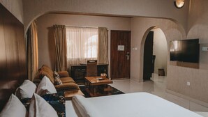 Habitación de hotel con cama, sofá, mesa de comedor, televisor y puerta que da a otra habitación.