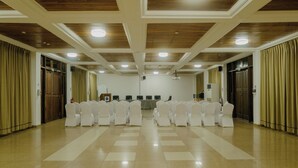 Un salón amplio con filas de sillas blancas, paneles de techo de madera y suelo a cuadros.