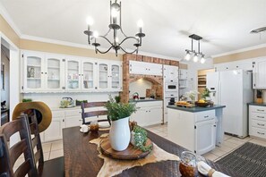 A modern kitchen with white cabinets, a brick backsplash, and a central island with a white pitcher and plants.
