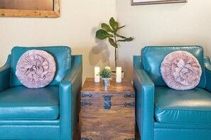 Two teal leather chairs with floral cushions, a small wooden table with a plant and candles, and a framed picture on the wall. - Long Live Cowboys!  3-Bed 2-Bath Near ACU and Expo (Abilene)
