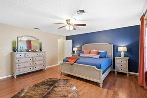Ein Schlafzimmer mit einem Bett, einem Schminktisch, Nachttischen, einem Deckenventilator und einem Teppich.