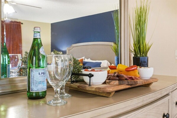 A room with a bed, a wooden side table with a bottle, a glass, and a fruit platter.