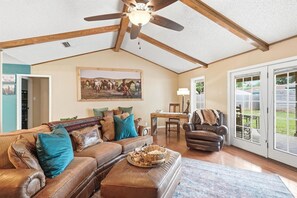 A spacious living room with a ceiling fan, a large painting, a leather sofa, and a dining area.