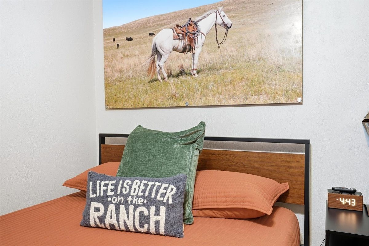 A bedroom with a bed, pillows, a wall clock, and a painting of a horse.