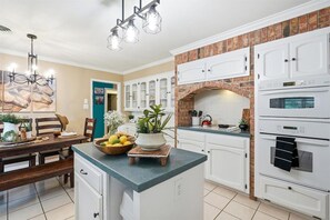 A kitchen with white cabinets, a brick backsplash, and a double oven.