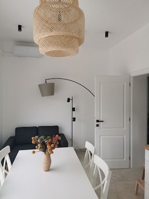 Ein zeitgemäßer Wohnraum mit einem weißen Tisch, einer gewobenen Lampe, einer schwarzen Stehlampe, einer weißen Tür und einem schwarzen Sofa.