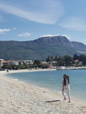 Ein Strand mit einem Berg im Hintergrund, klarem Himmel und einigen Gebäuden entlang der Küste.
